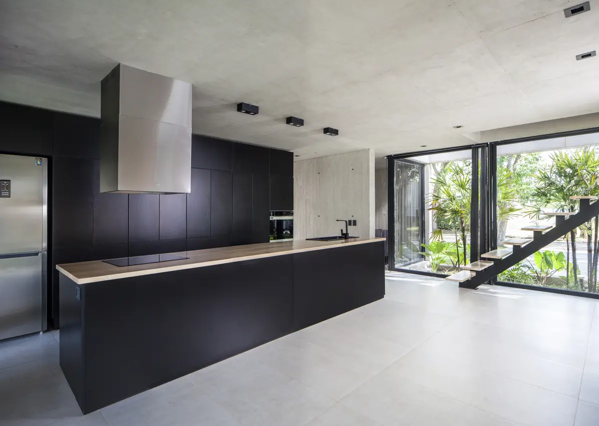 Cocina moderna abierta con isla negra y vista al jardín — proyecto Black House, por V2 Arquitectos, en City Bell