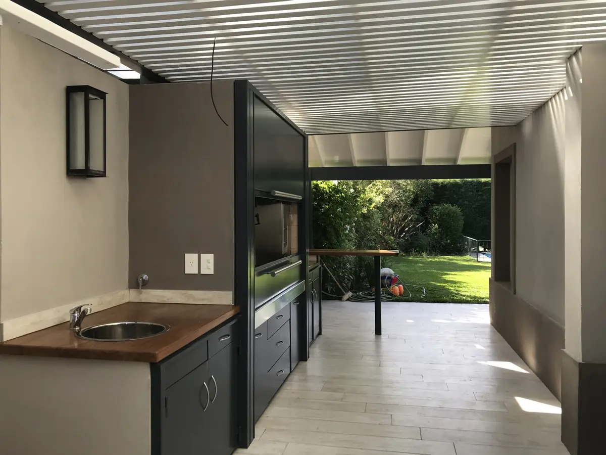Quincho moderno con parrilla empotrada y techo metálico — proyecto Casa Beccar, por Rioja Arquitectura, en Béccar
