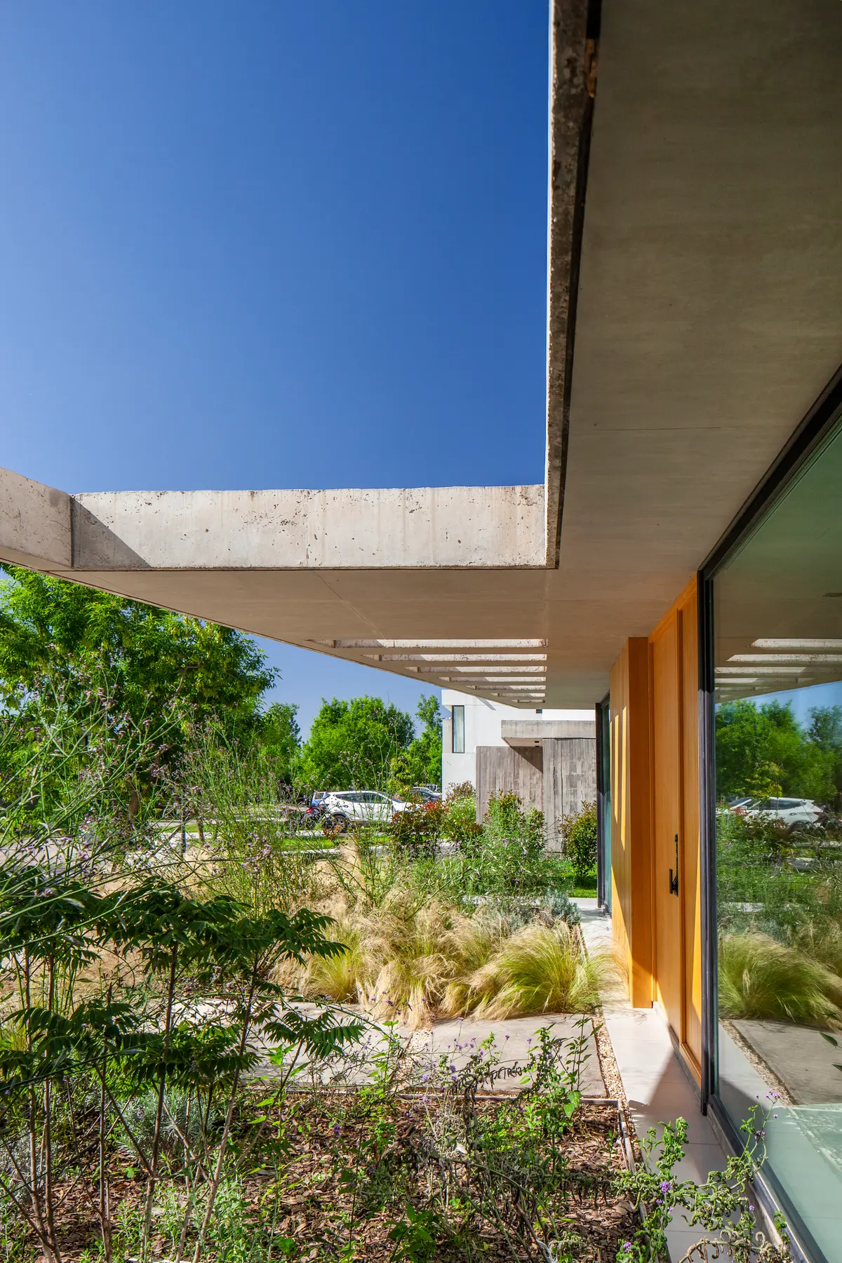Fachada moderna com concreto aparente e vegetação exuberante — projeto Casa ALVA, por V2 Arquitectos, em City Bell