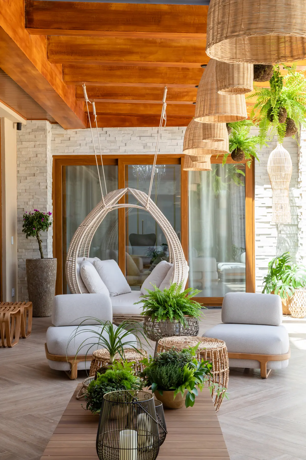 Terraza semi-cubierta con mobiliario de ratán, vigas de madera y plantas — proyecto Projeto Destaque Club&Casa, por OKA ARQUITETURA