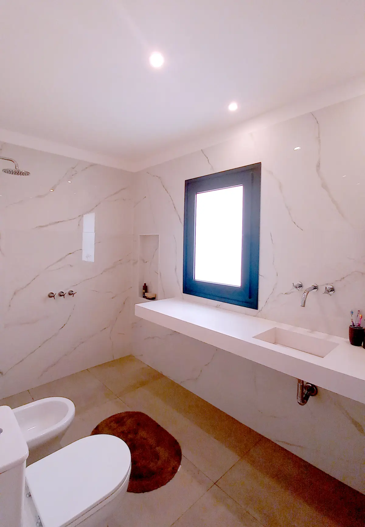 Baño moderno con paredes de mármol, mesada flotante y sanitarios blancos — proyecto Casa CG191, por EZ architects, en Belén de Escobar