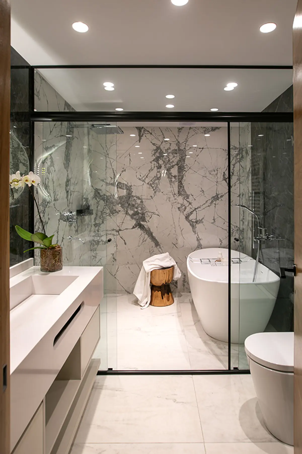 Baño moderno con mármol, banera blanca y ducha con cristal negro — proyecto Casa Oroño, por Estudio Plats, en Buenos Aires