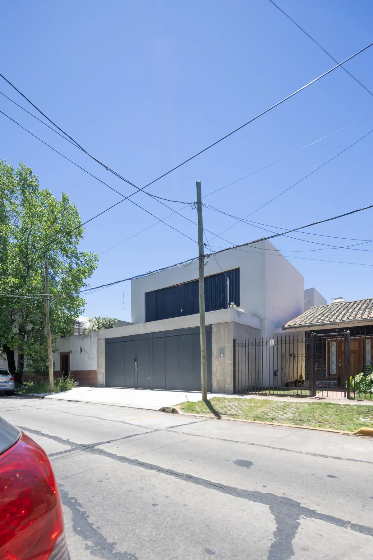 Fachada moderna con puerta de garaje metálica y grandes ventanas oscuras — proyecto CASA OrBa, por Alfredo Orfila arquitectura, en San Isidro