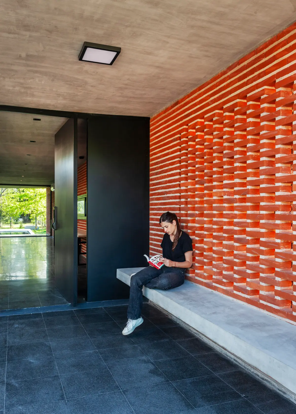 Parede de tijolos vazados, banco de concreto e porta pivotante — projeto Casa FLOIG, por V2 Arquitectos, em Villa Elisa