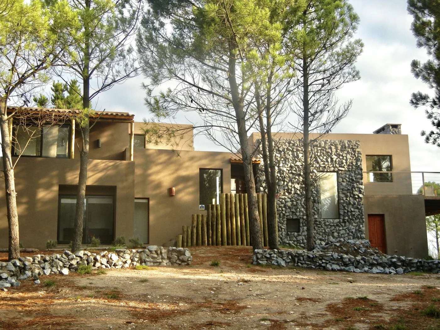 Fachada moderna de casa en piedra y madera con mucha vegetación