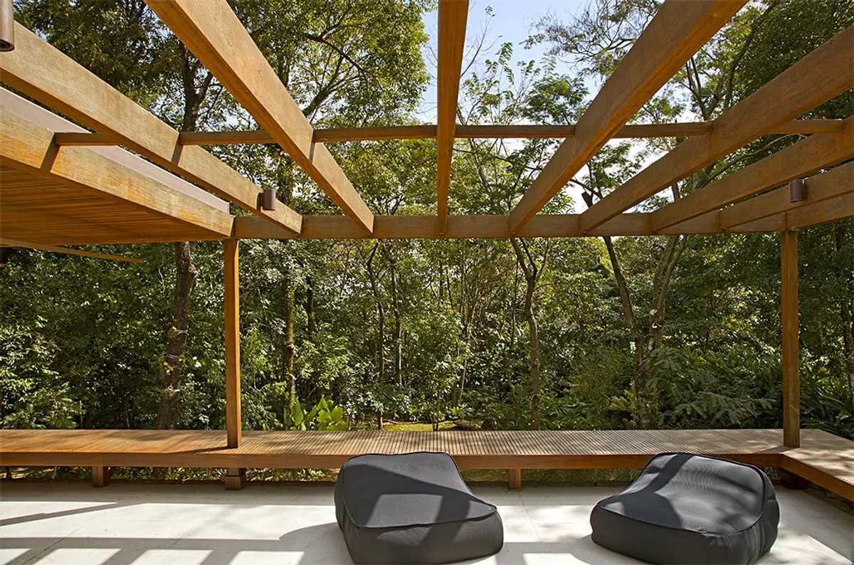 Quincho moderno con pérgola de madera y vista al bosque, muebles oscuros — proyecto Residência GS, por Gil Fialho