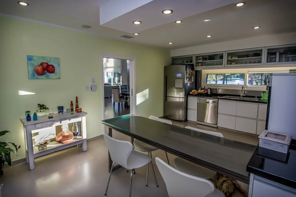 Cozinha moderna com sala de jantar integrada, paredes verdes, armários brancos e mesa escura — projeto Vivienda Unifamiliar en Pinamar, por Estudio Schifano, em Pinamar