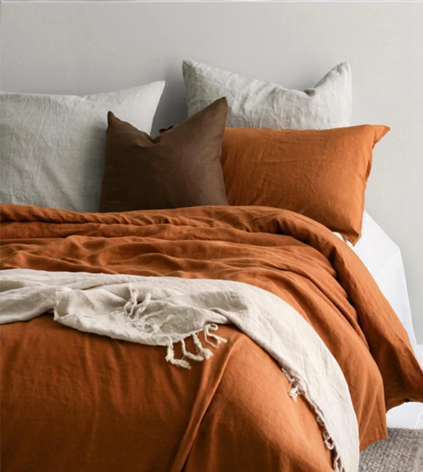 Dormitorio con cama de lino en tonos tierra, mantas y almohadas.
