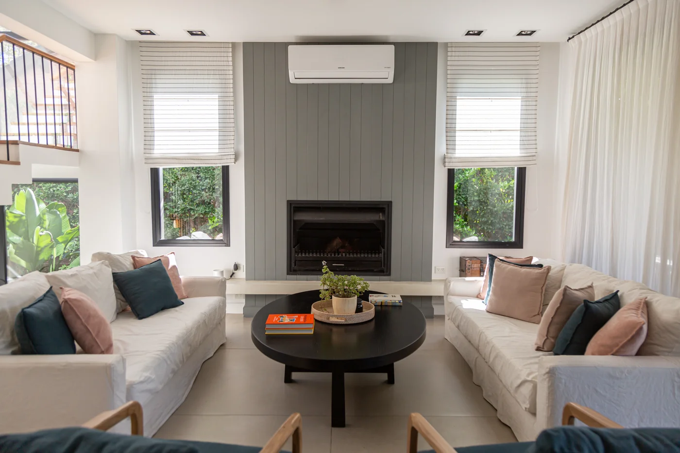 Living moderno con chimenea, paneles grises y mucha luz natural.