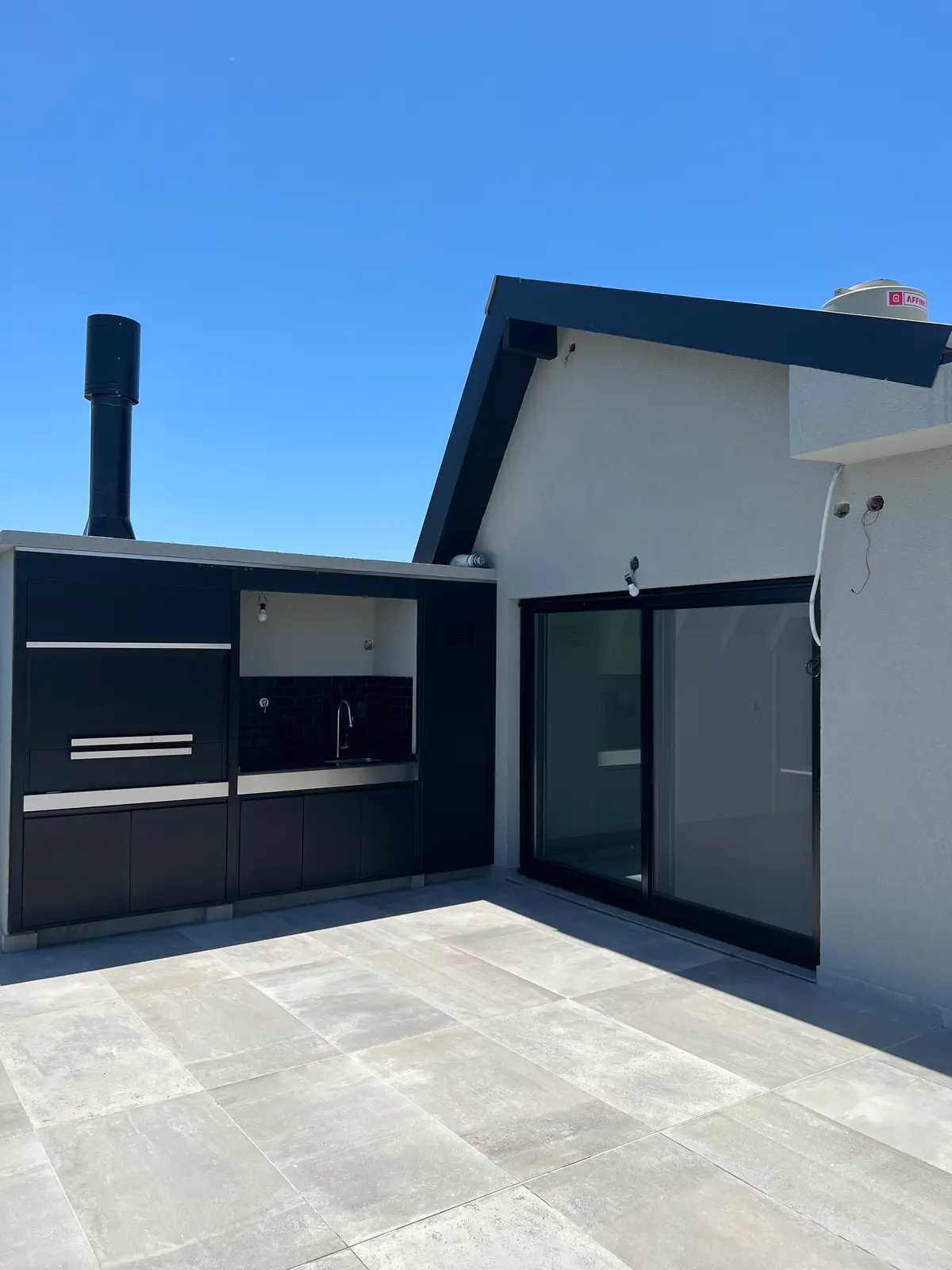 Área de churrasco moderna com piso de pedra e céu azul — projeto DEPTO MARTINEZ, por Estudio Grupo 32, em Martínez