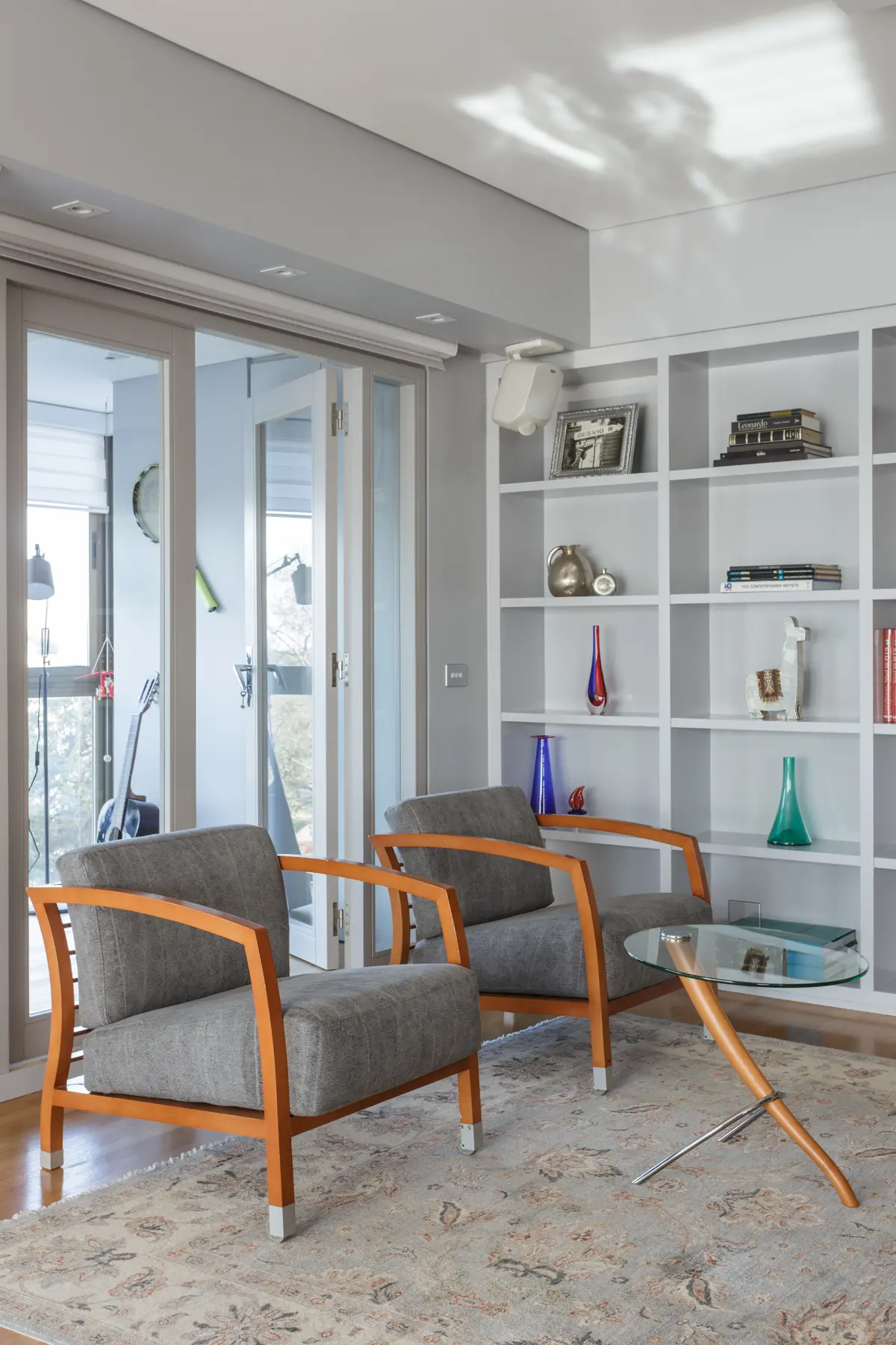 Sala de estar moderna com poltronas cinzas, estante branca e mesa de centro de vidro — projeto Piso en Belgrano, por Gutman+Lehrer Arquitectas, em Belgrano