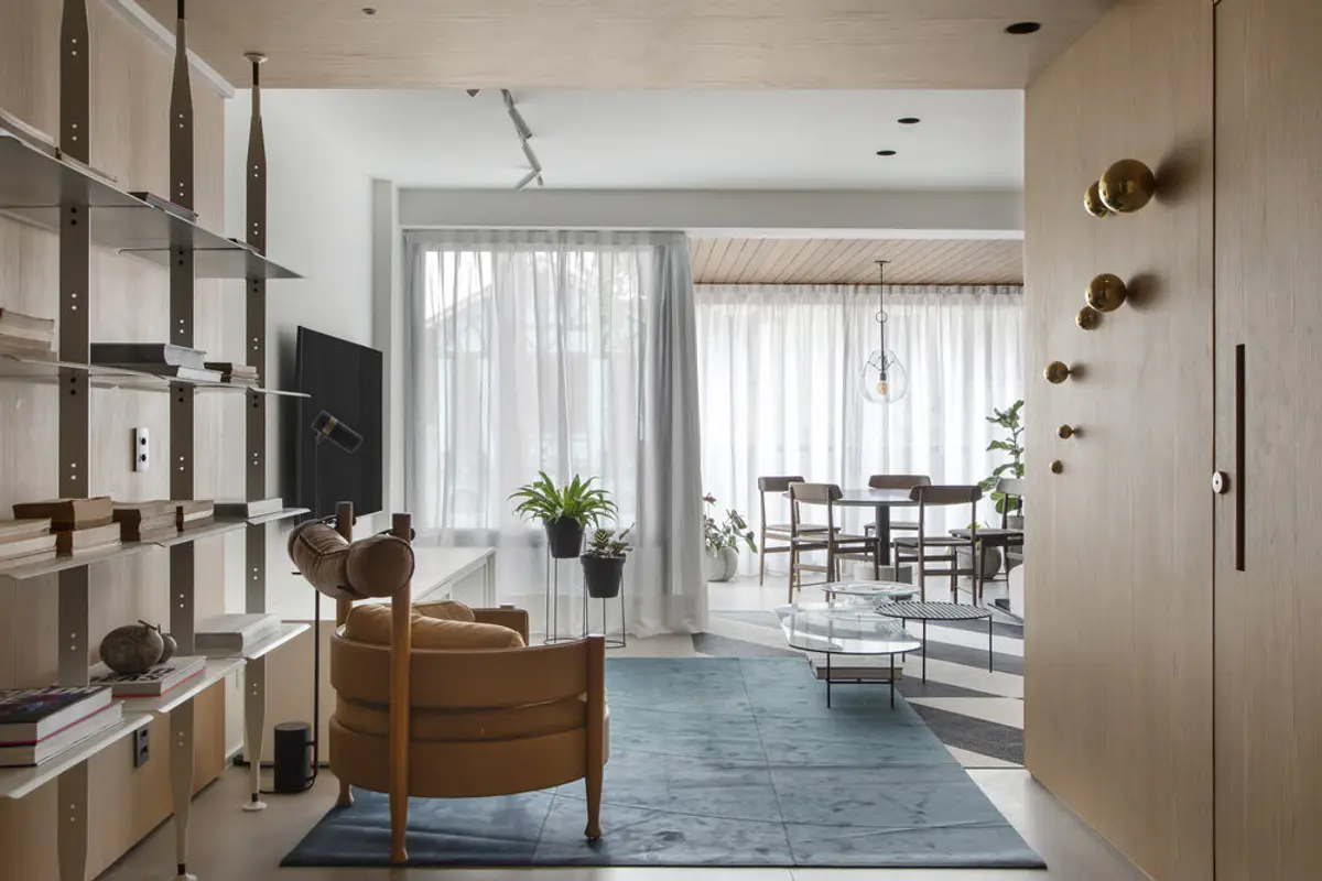 Pasillo moderno con estantería flotante y sillón caramelo junto a ventanal — proyecto MN House, por Studio Ro-ca