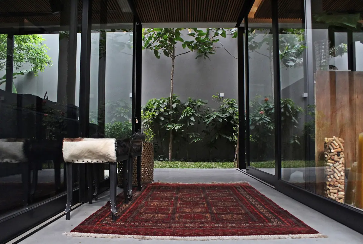 Galería moderna con ventanales negros, alfombra bordo y vista a patio con plantas — proyecto Residência HC, por Gil Fialho