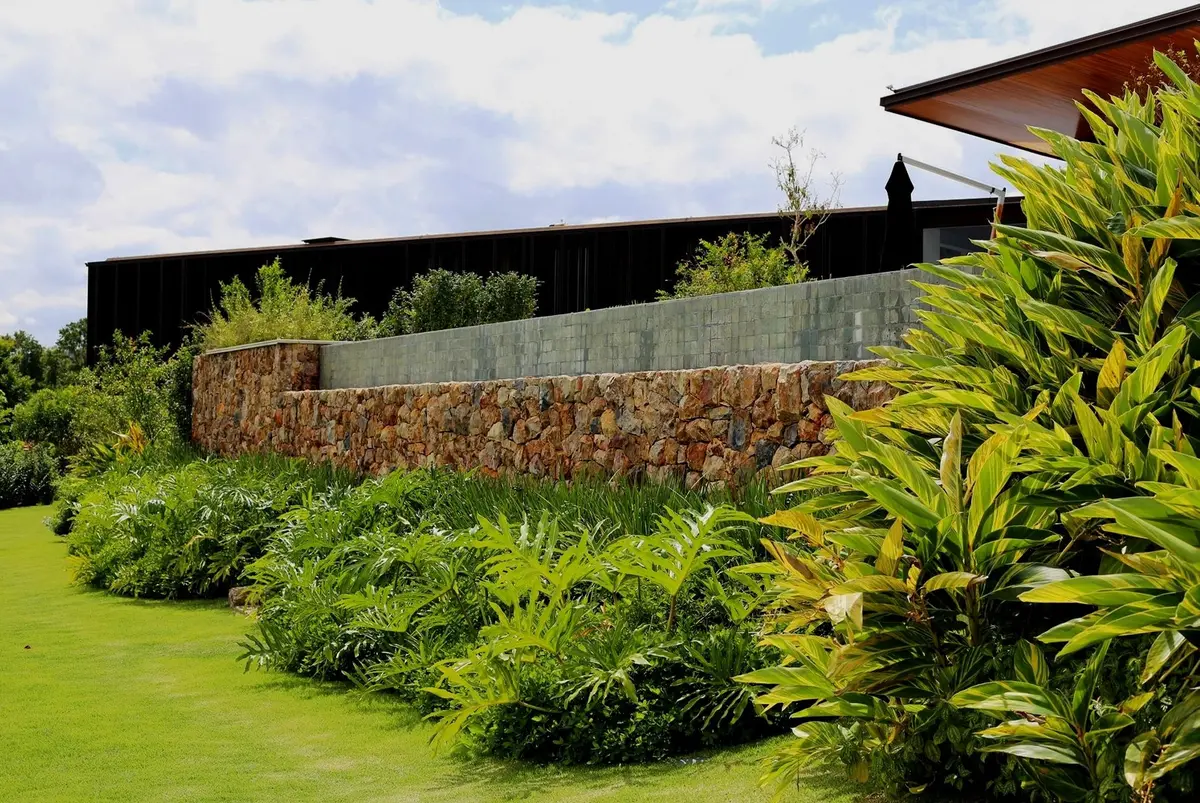Jardín moderno con muro de hormigón, plantas tropicales y césped impecable — proyecto Residência CA, por Gil Fialho