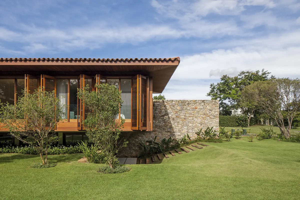 Casa moderna con fachada de madera y piedra, amplio jardin verde — proyecto Residência GS, por Gil Fialho