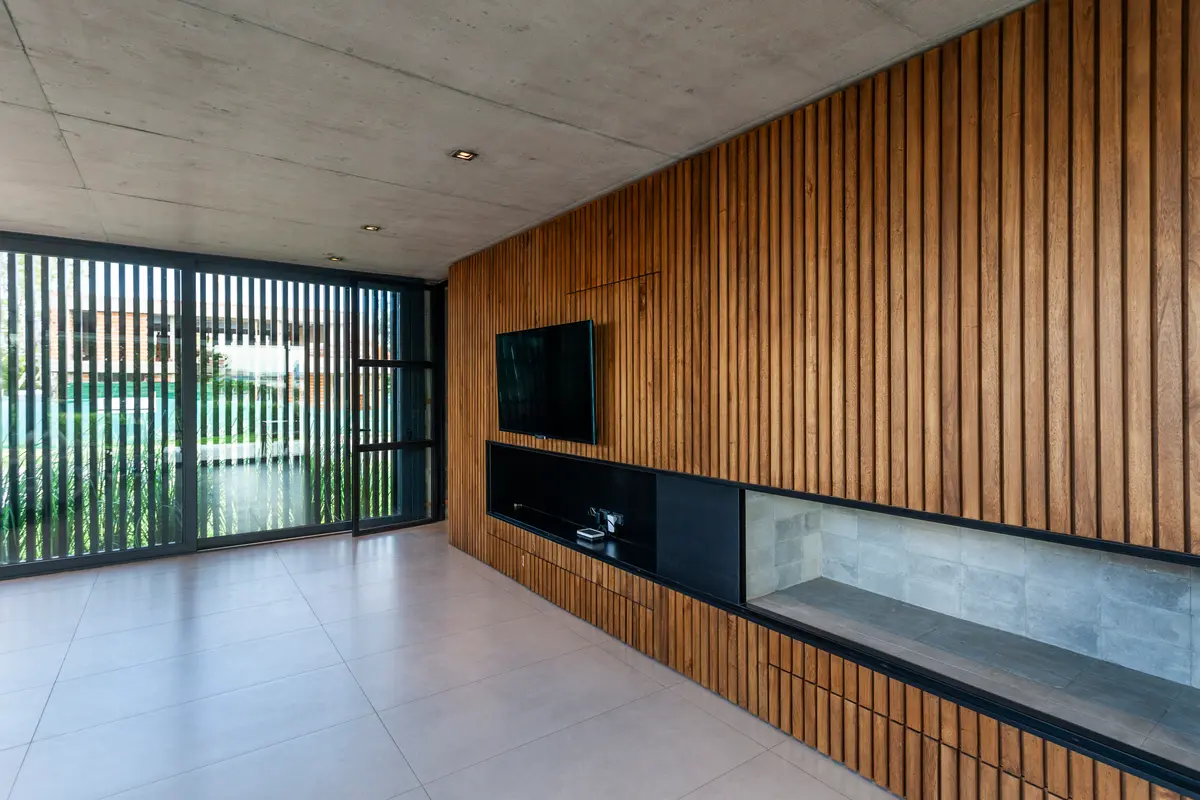 Living moderno con pared de listones de madera y estanterías de vidrio — proyecto Casa GUGA, por V2 Arquitectos, en City Bell