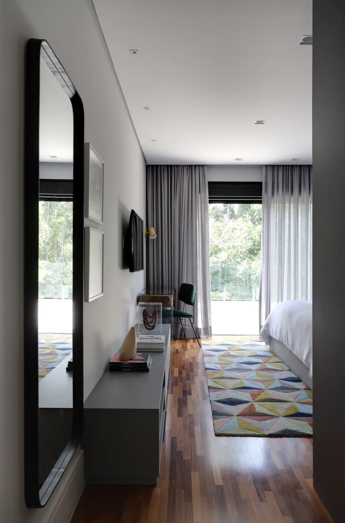 Quarto moderno com piso de madeira, tapete geométrico e vista para o jardim — projeto Projeto Destaque Club&Casa, por Barbara Dundes – Arquitetura + Design