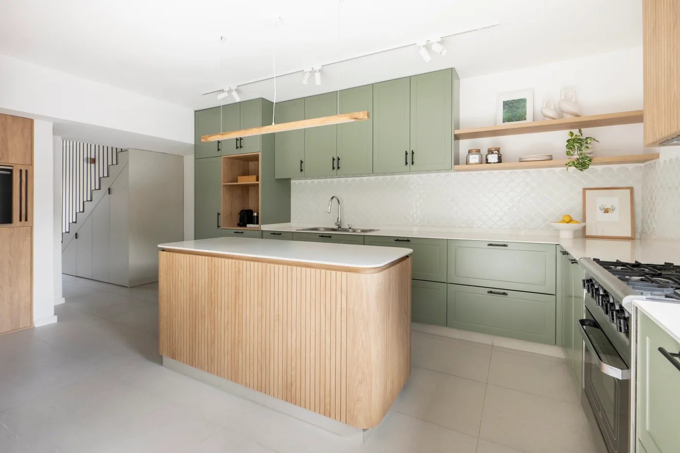 Cocina moderna con isla curva de madera y muebles verdes.