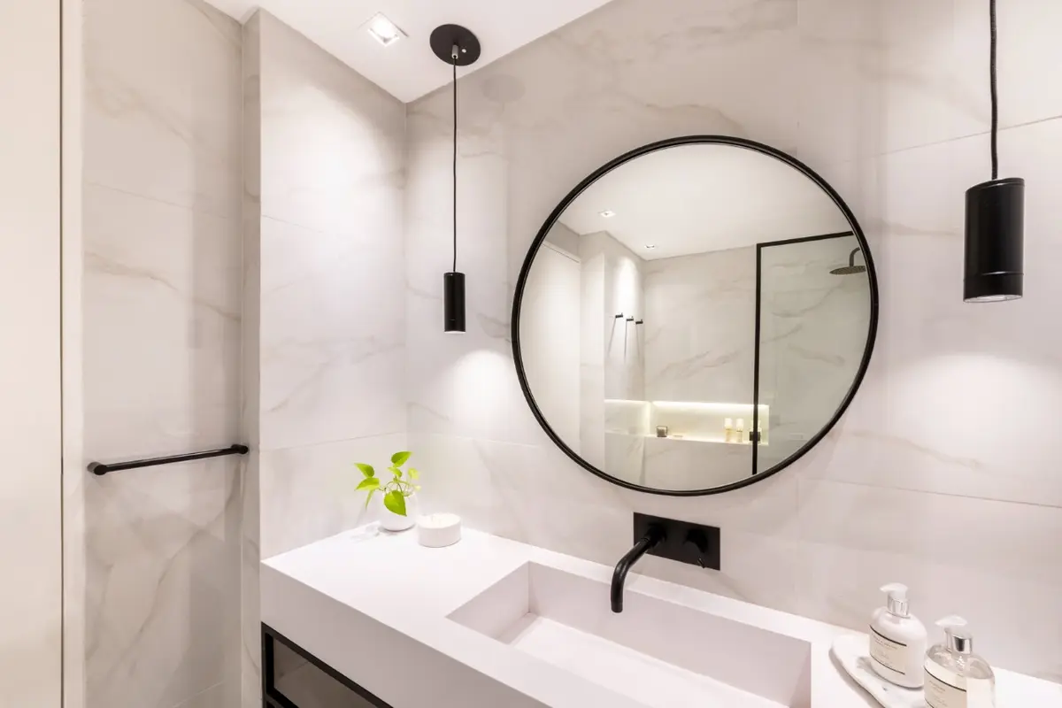 Baño moderno con espejo redondo, grifería negra y paredes de mármol — proyecto Libertad, por Estudio Basa, en Buenos Aires