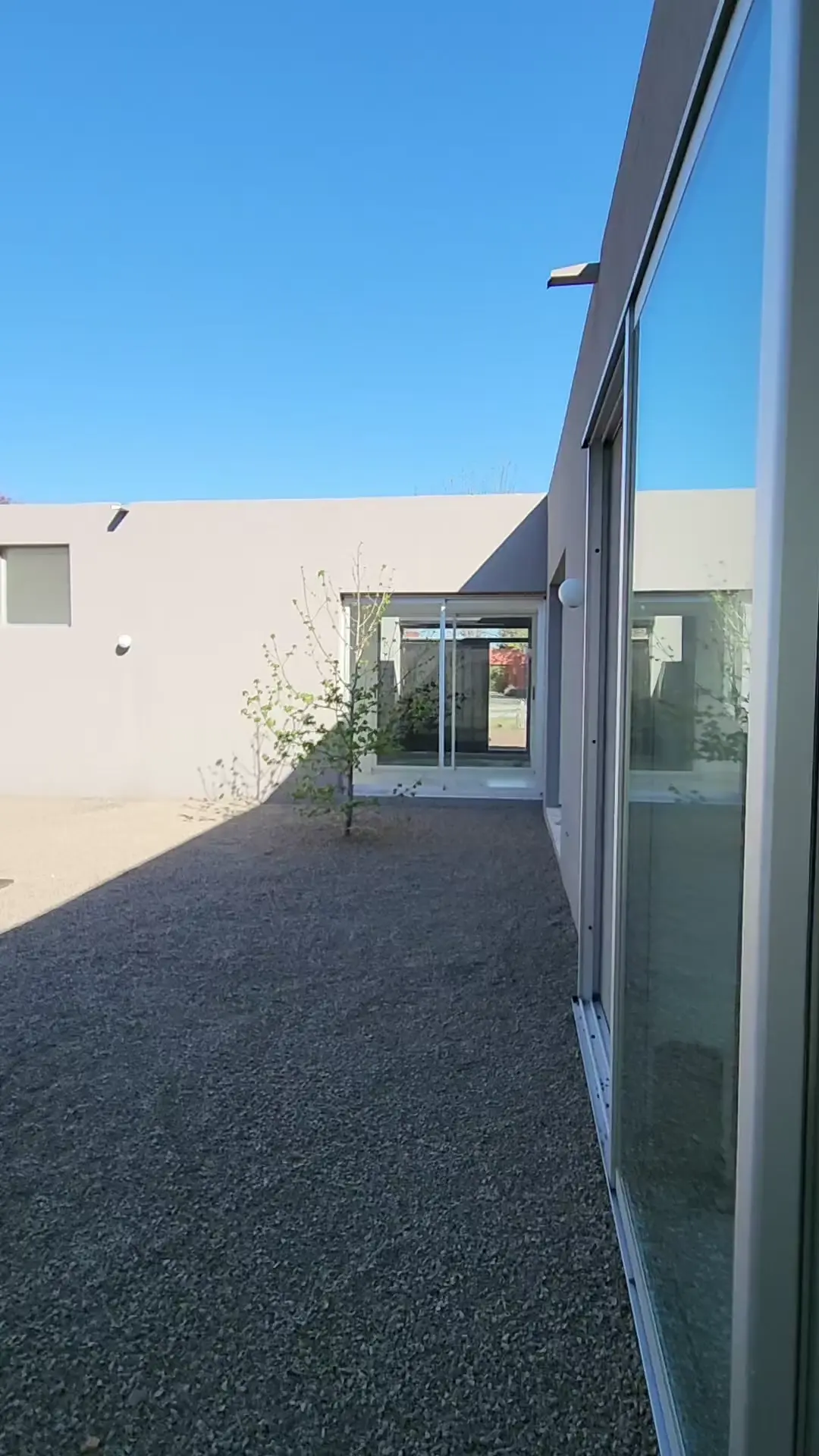 Fachada moderna con patio de grava y grandes ventanales de cristal — proyecto Casa VAL, por Estudio Rifahi, en Capilla del Señor